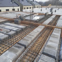 VITA-BUD - Zbrojenie stropu Teriva z betonowych pustaków szalunkowych, widok z góry na budowę domu jednorodzinnego w pochmurny dzień. Elementy konstrukcyjne w bliskiej perspektywie.