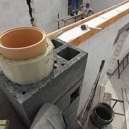 VITA-BUD - Wznoszenie komina z pustaków szalunkowych na budowie domu. Widoczne białe bloczki Ytong, drewniane szalunki, drabina i narzędzia murarskie.