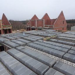 VITA-BUD - Wznoszenie stropu Teriva na budowie domu w Brzegu Dolnym. Widoczne pustaki stropowe i zbrojenie, w tle wzniesione ściany z czerwonej cegły.