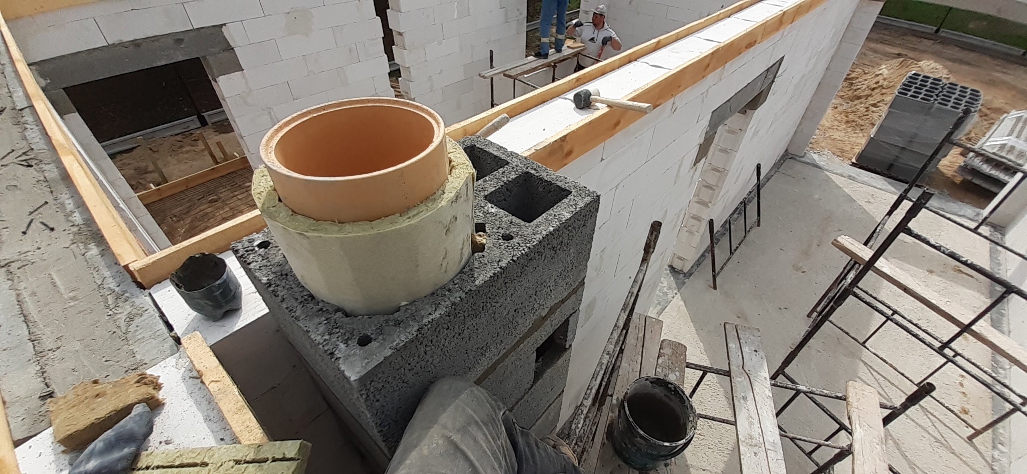 Wznoszenie komina z pustaków szalunkowych na budowie domu. Widoczne białe bloczki Ytong, drewniane szalunki, drabina i narzędzia murarskie.