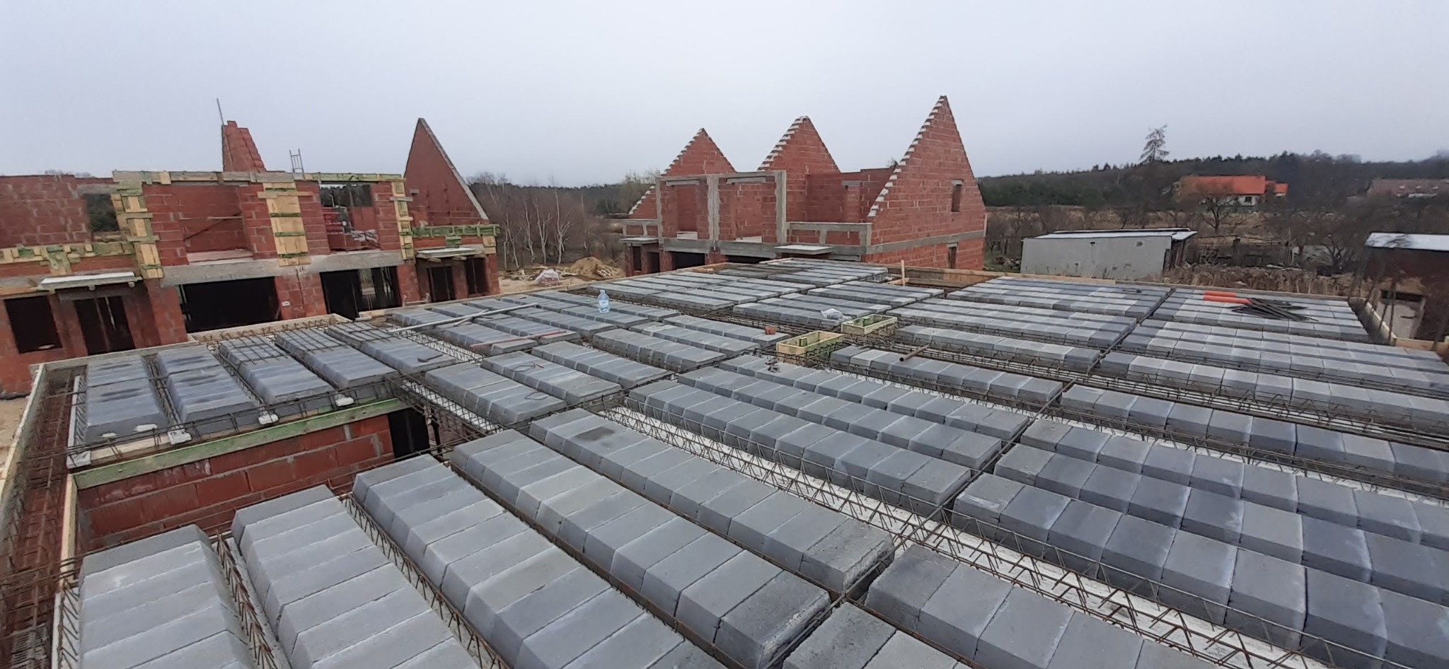 Wznoszenie stropu Teriva na budowie domu w Brzegu Dolnym. Widoczne pustaki stropowe i zbrojenie, w tle wzniesione ściany z czerwonej cegły.