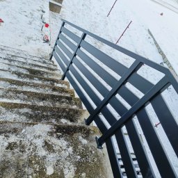 13th Welding Garage - Częściowy widok nowo zamontowanej, czarnej, metalowej balustrady schodowej z profilami poziomymi, prowadzącej w dół po betonowych schodach zewnętrznych pokrytych śniegiem, z narzędziami montażowymi...
