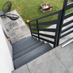13th Welding Garage - Nowoczesne schody zewnętrzne z szarymi stopniami i czarną, metalową balustradą na tle zadbanego trawnika z elementami rekreacyjnymi.
