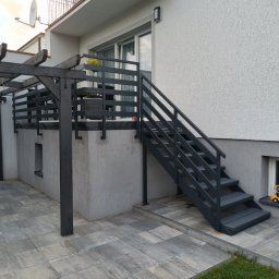 13th Welding Garage - Zewnętrzne schody metalowe w grafitowym kolorze, prowadzące na balkon z pergolą. Nowoczesny wygląd, kostka brukowa i fragment trawnika. Elegancka architektura.