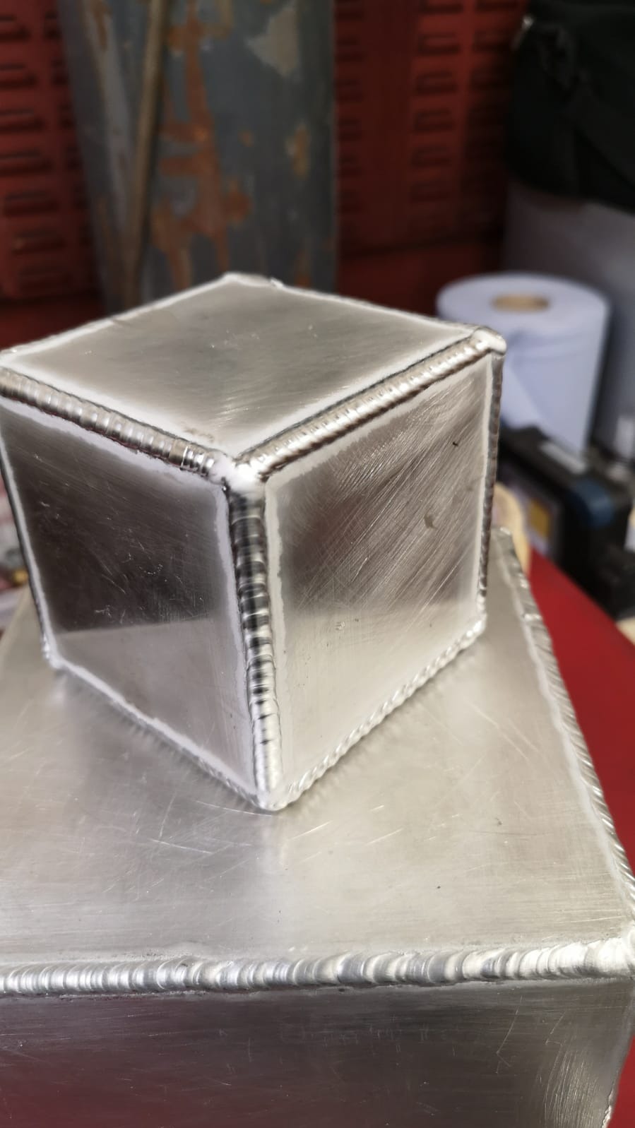 Dwa aluminiowe, spawane prostopadłościany, jeden na drugim, z widocznymi śladami obróbki i spoinami