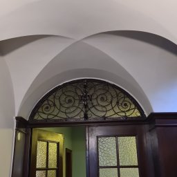 DoMpro- Remonty I Wykończenia wnętrz - Drewniane drzwi z ozdobną, metalową kratą w górnej części, widoczne pod łukowatym sufitem.