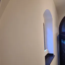 Wnętrze z łukowatym oknem i świeżo pomalowaną, gładką ścianą w odcieniach bieli, widoczne detale wykończeniowe i architektoniczne.