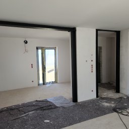 DoMpro- Remonty I Wykończenia wnętrz - Wnętrze w trakcie prac wykończeniowych: ściany przygotowane do malowania, widoczne instalacje elektryczne i zabezpieczone drzwi balkonowe.
