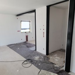 DoMpro- Remonty I Wykończenia wnętrz - Wnętrze w trakcie remontu: białe ściany, czarne metalowe ramy, zabezpieczona podłoga, widoczne instalacje, drabina malarska. Stan surowy, przygotowanie do dalszych prac wykończeniowych.