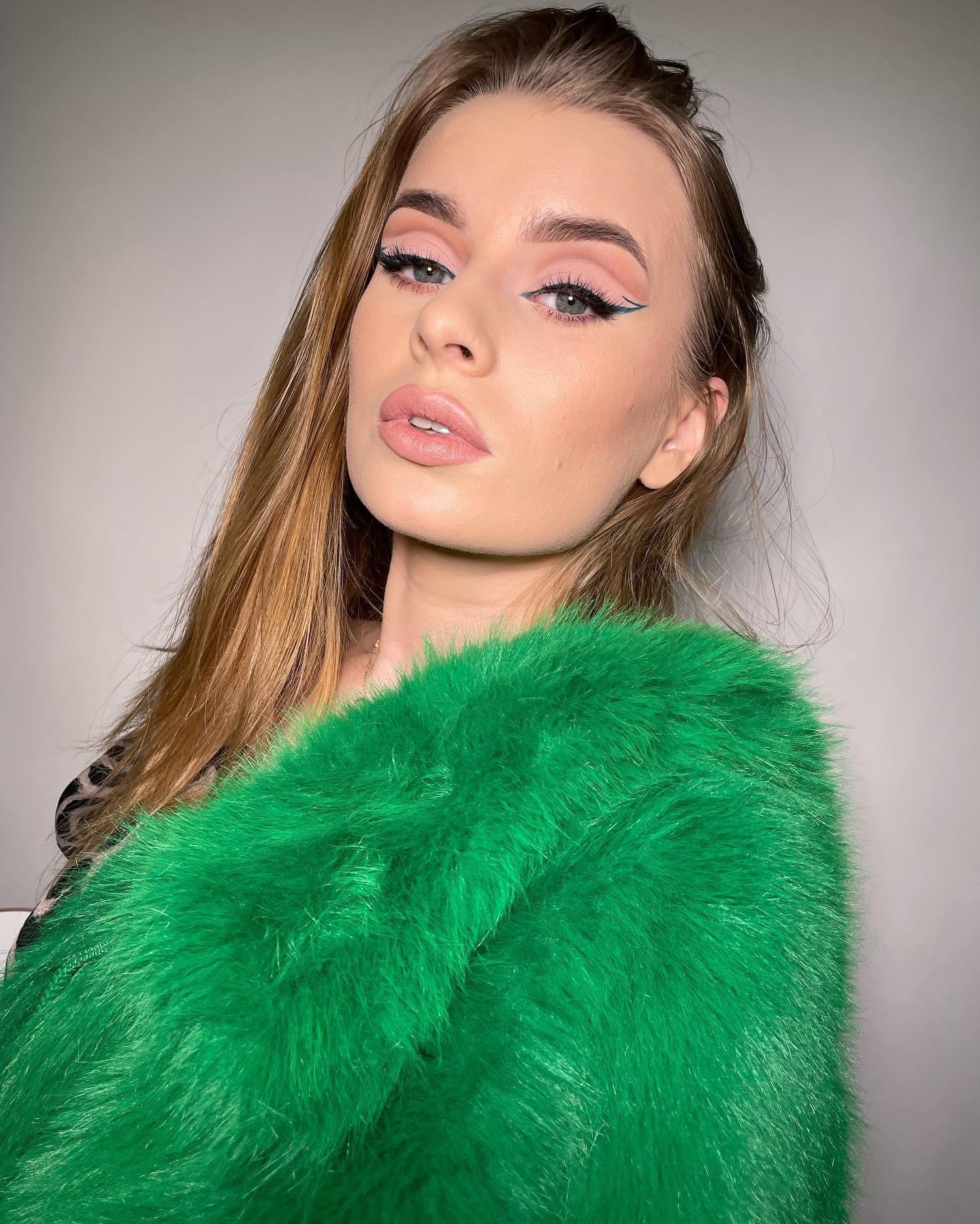 Portret kobiety z profesjonalnie wykonanym delikatnym makijażem oczu z zieloną kreską i podkreślonymi ustami, ubrana w jaskrawo zielone futro.