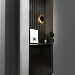 Nowoczesna, monochromatyczna łazienka z czarną szafką pod umywalką, okrągłym kinkietem i minimalistyczną grafiką z motywem roślinnym, widoczna przez częściowo otwarte drzwi.