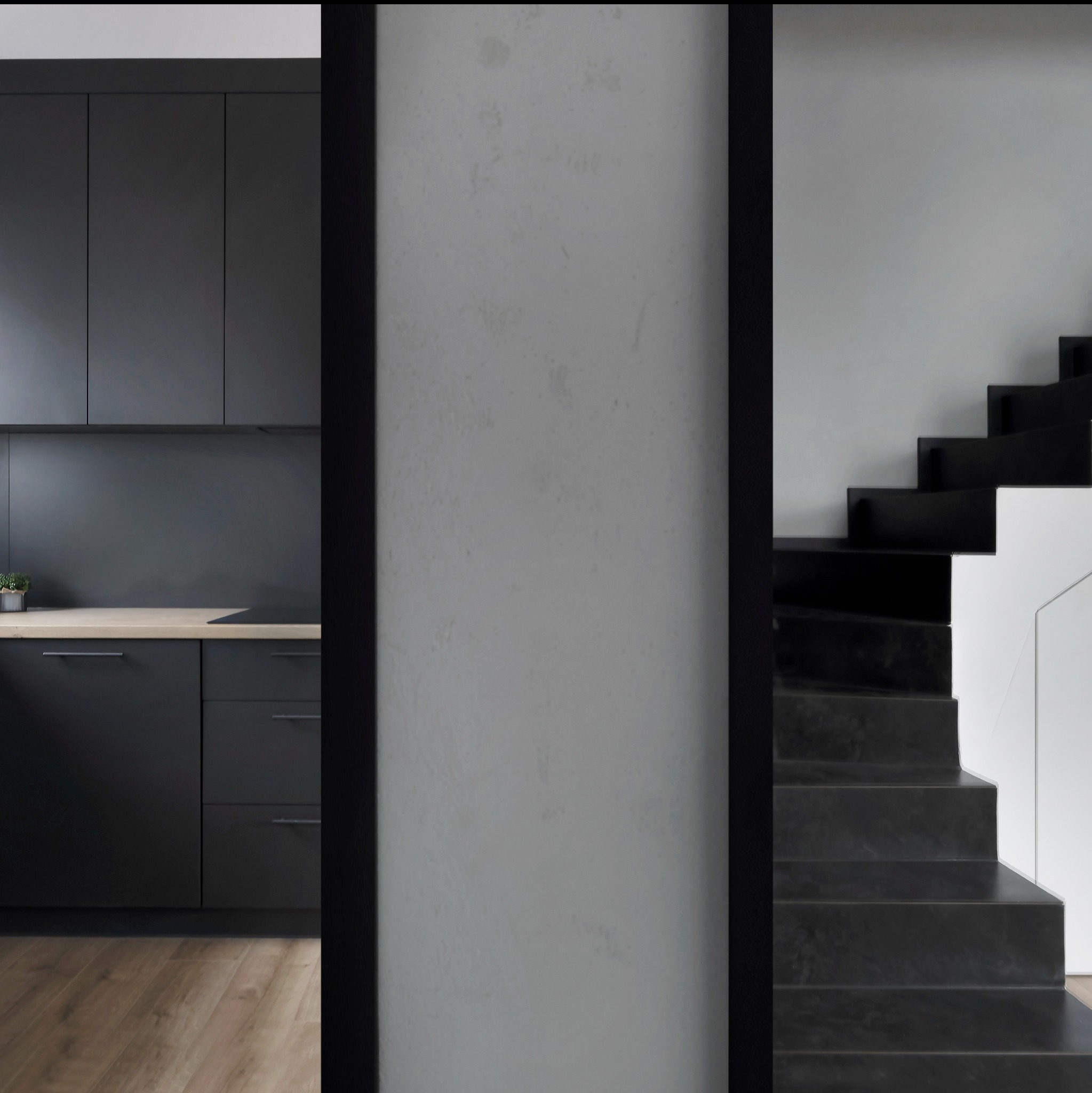 Nowoczesna kuchnia z czarnymi szafkami i drewnianym blatem, widok na czarne schody z białymi akcentami przez framugę drzwi.