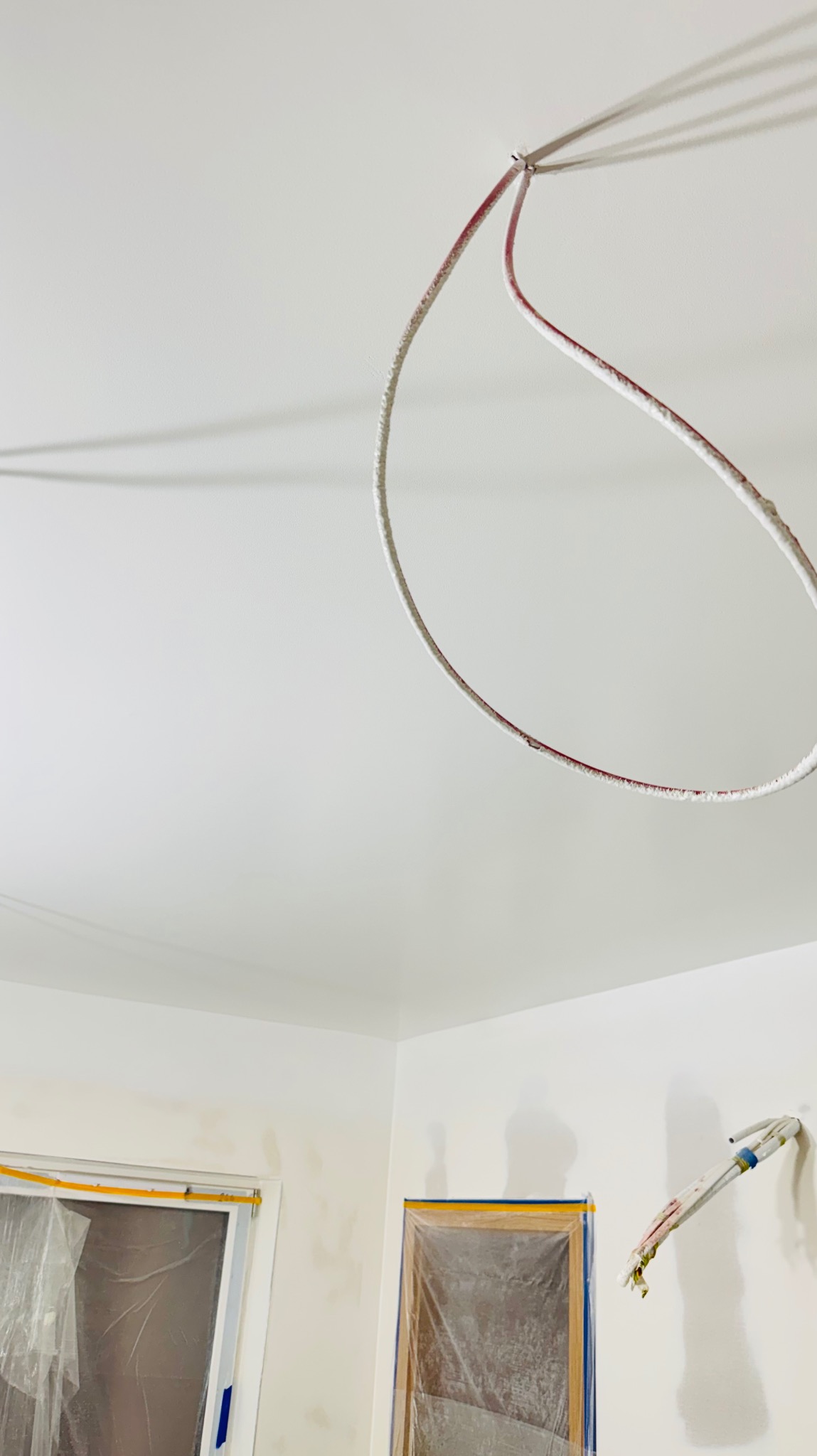 Białe ściany po szpachlowaniu, z widocznymi przewodami elektrycznymi i zabezpieczonymi oknami folią malarską. Przygotowanie do malowania.