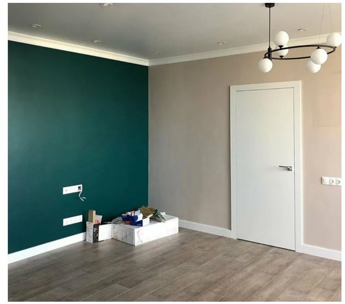 Pomieszczenie po malowaniu ścian na butelkową zieleń i beż, z ułożonymi panelami podłogowymi. Widoczna biała listwa przypodłogowa, białe drzwi i nowoczesna lampa.