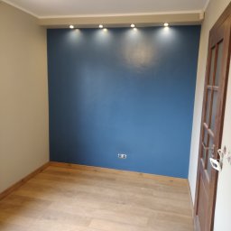 ART-BUD Usługi ogólnobudowlane - Pomalowane na niebiesko wnętrze pokoju z jasną podłogą, oświetleniem punktowym i drewnianymi drzwiami z przeszkleniami.