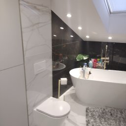 ART-BUD Usługi ogólnobudowlane - Nowoczesna łazienka z czarno-białymi marmurowymi płytkami, wiszącą toaletą, wolnostojącą wanną i oknem dachowym.