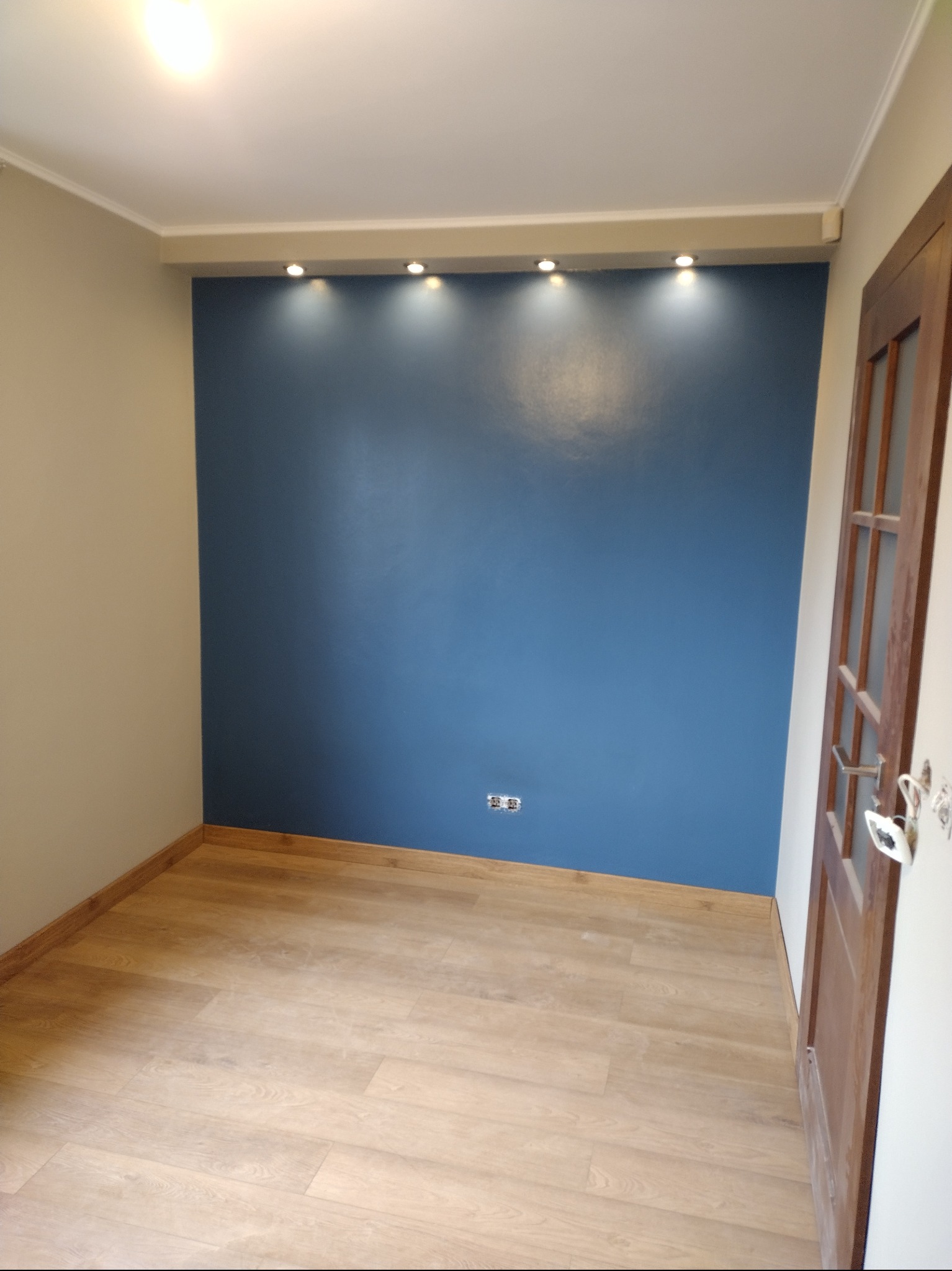 Pomalowane na niebiesko wnętrze pokoju z jasną podłogą, oświetleniem punktowym i drewnianymi drzwiami z przeszkleniami.