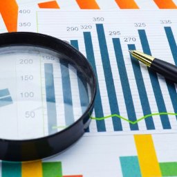 kredytylublin.pl - Kredyty, pożyczki, ubezpieczenia - Lupa i długopis na wydrukowanym wykresie słupkowym i liniowym z danymi liczbowymi, analiza danych finansowych.