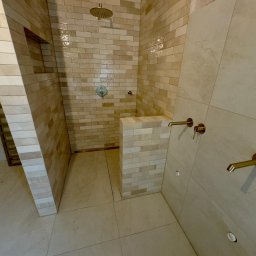Jakość Projekt Bud Anatolii Nechyporuk - Wykończony prysznic walk-in z beżowymi płytkami imitującymi cegłę, złotą armaturą i odpływem liniowym w podłodze.