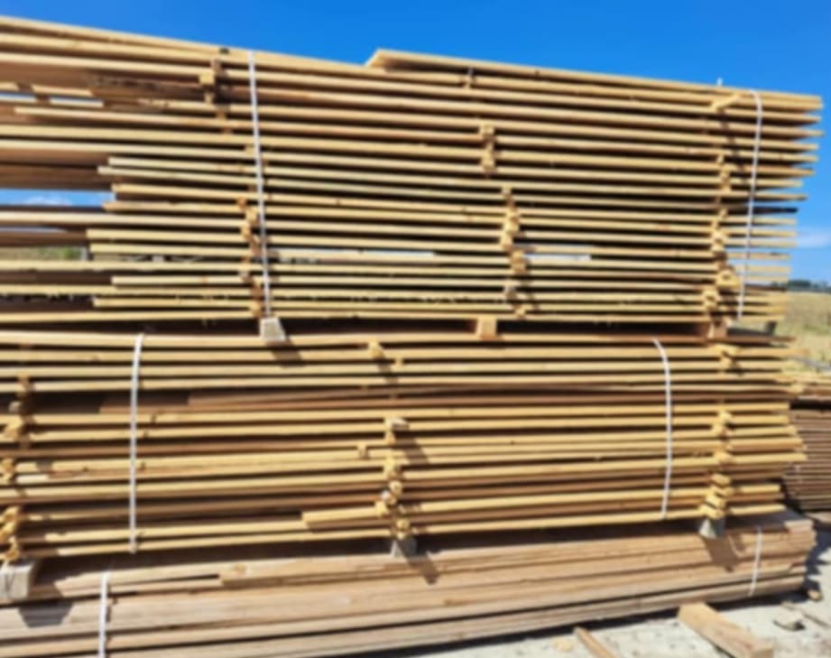 Stos desek tarcicy, spiętych białym sznurkiem, ułożonych na palecie pod błękitnym niebem.