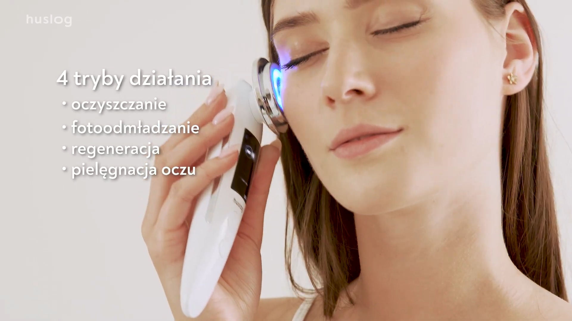 Kobieta stosuje na skórę twarzy białe urządzenie kosmetyczne z niebieskim światłem, oferujące 4 tryby działania: oczyszczanie, fotoodmładzanie, regenerację i pielęgnację oczu.