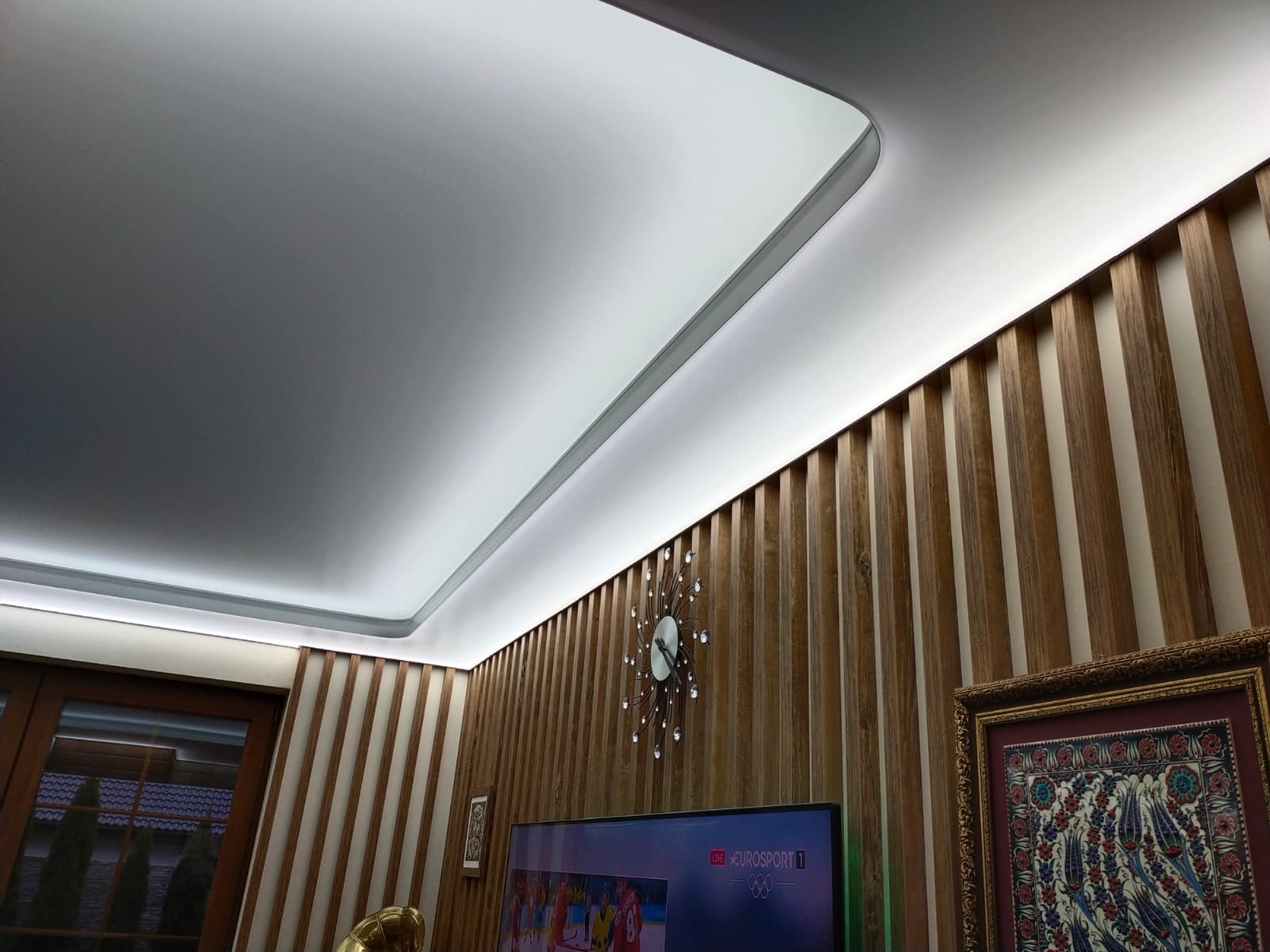 Nowoczesny pokój z białym, podświetlanym obniżonym sufitem i drewnianymi panelami ściennymi, widok z dołu.