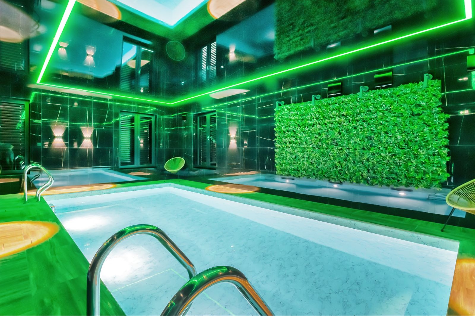 Nowoczesny basen w pomieszczeniu z czarnymi marmurowymi ścianami, zielonym oświetleniem LED i ścianą z roślin, widoczne metalowe poręcze wejścia do basenu.