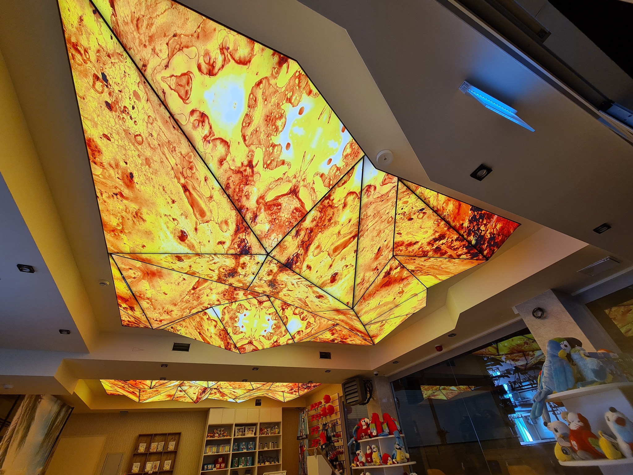 Pomarańczowo-żółty, podświetlany sufit z geometrycznym wzorem w pomieszczeniu sklepowym, widok z dołu.