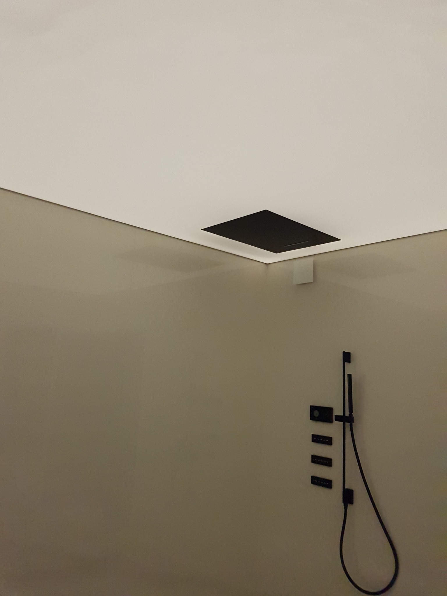 Biały, podwieszany sufit z czarnym, kwadratowym otworem wentylacyjnym i minimalistycznym oświetleniem LED w łazience z szarą ścianą i czarną armaturą prysznicową.