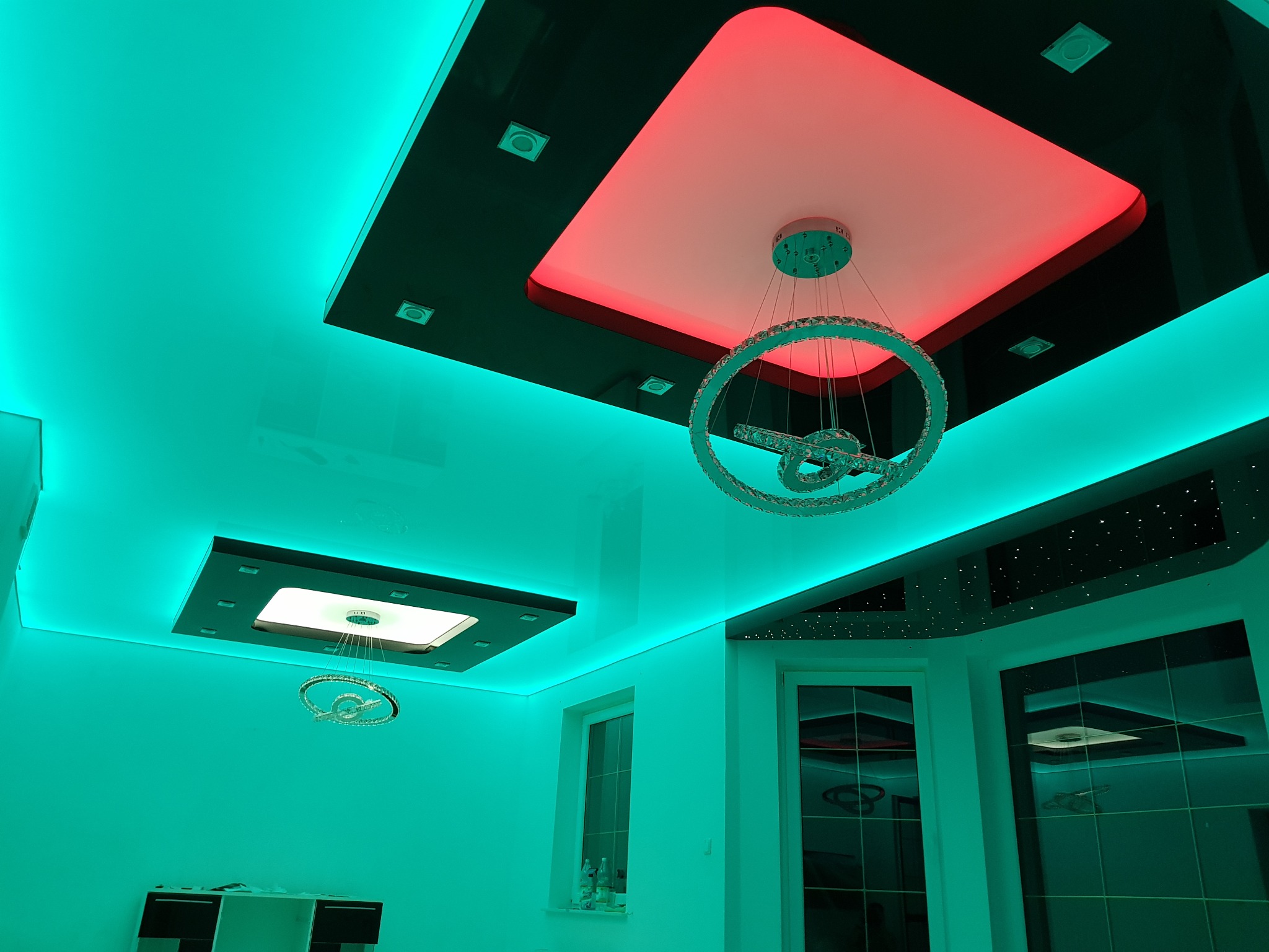 Nowoczesny sufit z podświetleniem LED w kolorach turkusowym i czerwonym, z wbudowanymi lampami i kryształowym żyrandolem