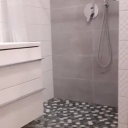 Nowoczesna łazienka z białą szafką umywalkową, szarą kabiną prysznicową z deszczownicą i mozaikową podłogą w strefie prysznica, przechodzącą w patchworkowe płytki podłogowe.