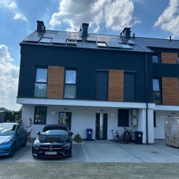 Energy 4 you Krzysztof Słomka - Nowoczesny szeregowiec z panelami słonecznymi na dachu, zaparkowane auta na podjeździe, błękitne niebo z chmurami w tle. Widok z poziomu gruntu.