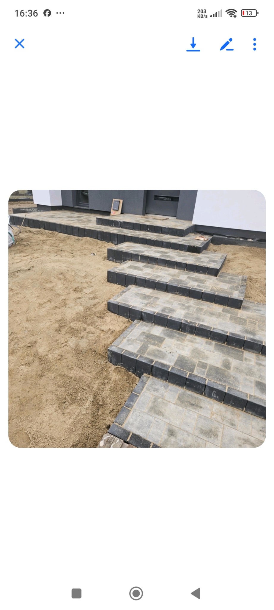 Ułożone schody z kostki brukowej prowadzące do domu. Widoczne piaskowe podłoże i fragment elewacji budynku. Detal: czarne obrzeża kostki.