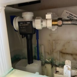 Hydro-mił Usługi Hydrauliczne - Spłuczka Geberit Typ 333 wewnątrz zbiornika, widoczne elementy instalacji wodnej i osad. Woda delikatnie cieknie z zaworu.