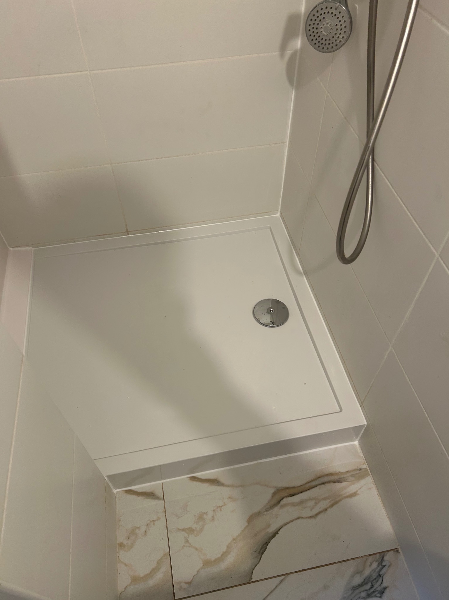 Biały brodzik z odpływem i słuchawką prysznicową w kabinie wyłożonej płytkami. Widok z góry, Warszawa.