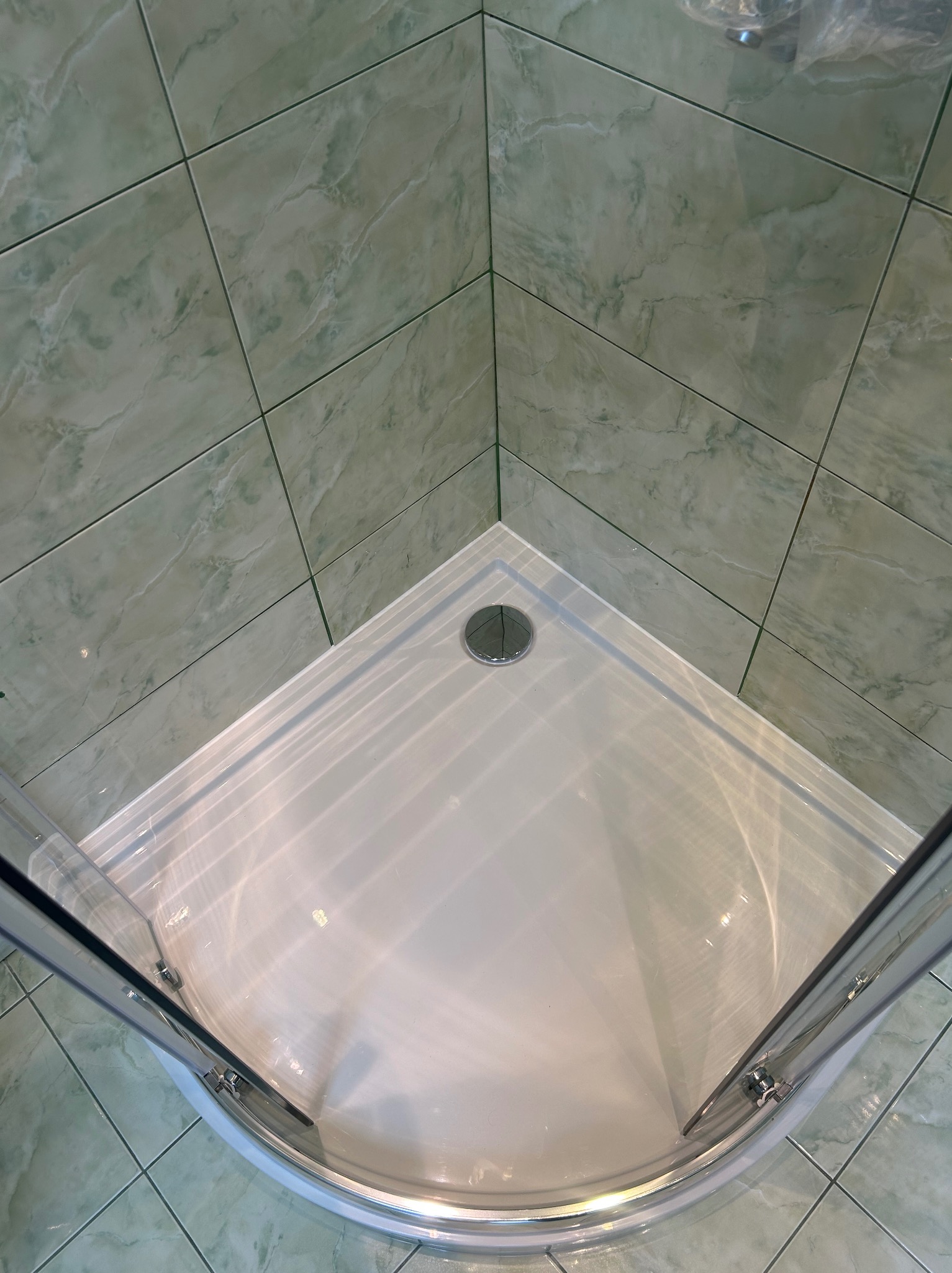 Narożna kabina prysznicowa z brodzikiem i zielonymi płytkami imitującymi marmur. Widok z góry na zamontowaną kabinę.