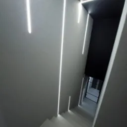 Minimalistyczne schody z oświetleniem LED wzdłuż ścian, prowadzące do pomieszczenia z przeszklonymi drzwiami, całość w odcieniach szarości i bieli.