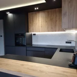 Nowoczesna kuchnia z czarnymi matowymi frontami i drewnianymi akcentami, podświetlana mozaika na ścianie, czarny blat i drewniany barek.