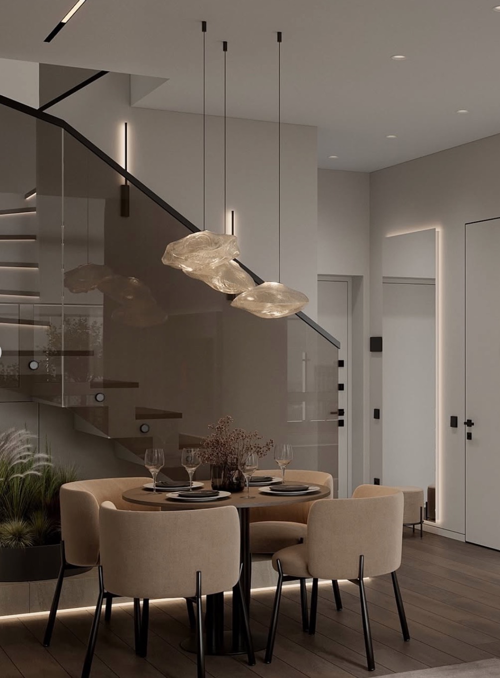 Elegancka jadalnia w neutralnych barwach: okrągły stół z nakryciem, beżowe krzesła, designerska lampa wisząca, schody z przeszkloną balustradą i dekoracyjne oświetlenie.