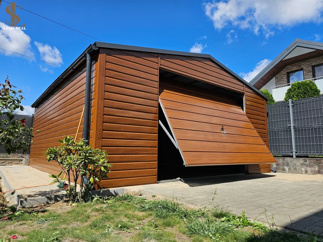 Blaszany garaż z częściowo otwartą, segmentową bramą w kolorze drewna, widoczny z boku na tle kostki brukowej i trawnika, z logo firmy w lewym górnym rogu.