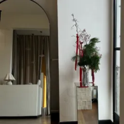 Eleganckie lustro łukowe w czarnej ramie odbija wnętrze salonu. Dekoracja świąteczna na lustrzanym postumencie dodaje uroku. Parkiet w ciepłym odcieniu brązu.