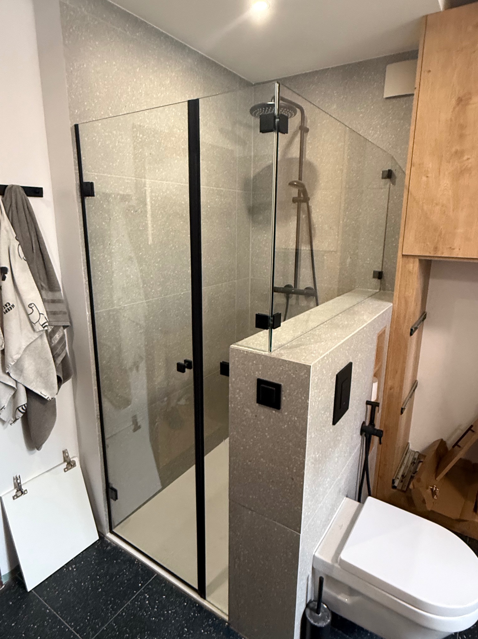 Nowoczesna kabina prysznicowa ze szkła hartowanego z czarnymi profilami, szara mozaika na ścianach, minimalistyczny design łazienki.