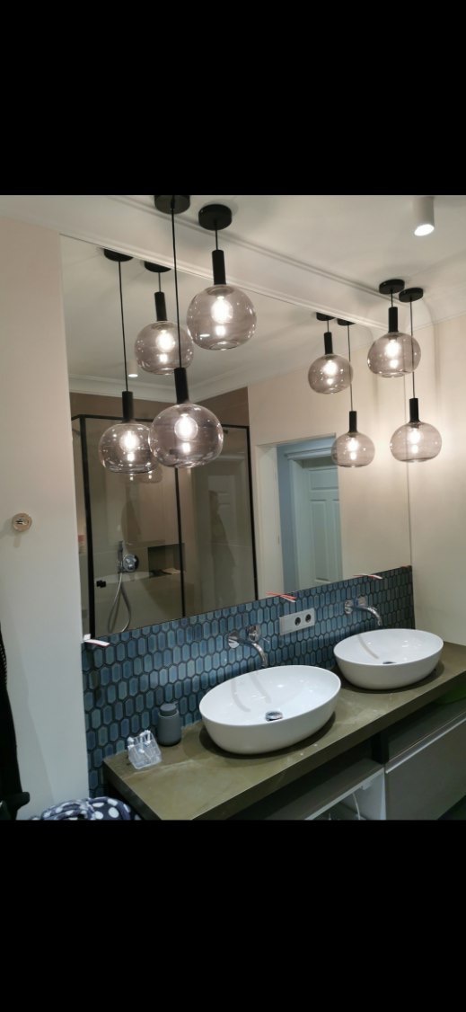 Nowoczesna łazienka z owalnymi umywalkami, mozaiką i dużym lustrem, w którym odbijają się szklane lampy wiszące.