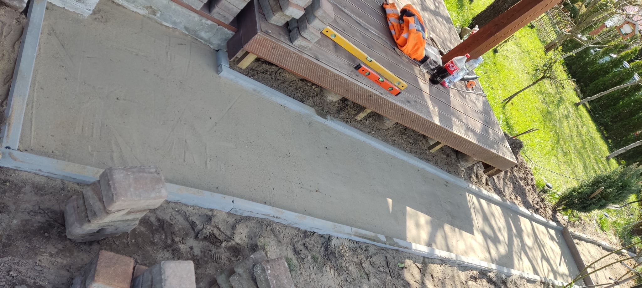 Przygotowany podkład z piasku i cementu pod kostkę brukową, obramowany metalowymi profilami, z widocznymi narzędziami pracy i stosem kostki obok.