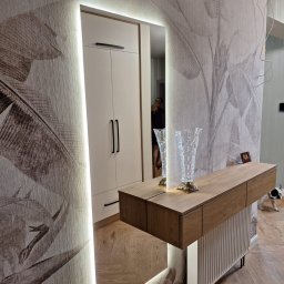 WAMA Wojciech Świątek - Nowoczesne wnętrze z szafą wnękową w lustrzanym odbiciu, podświetlanym LED, z drewnianą konsolą i wzorem liści na tapecie. Uwagę przykuwa pies w tle.