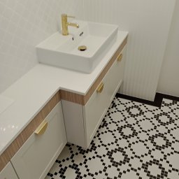 WAMA Wojciech Świątek - Biała szafka łazienkowa na wymiar z blatem, złotą armaturą i uchwytami, na tle wzorzystej podłogi. Umywalka prostokątna, nablatowa.