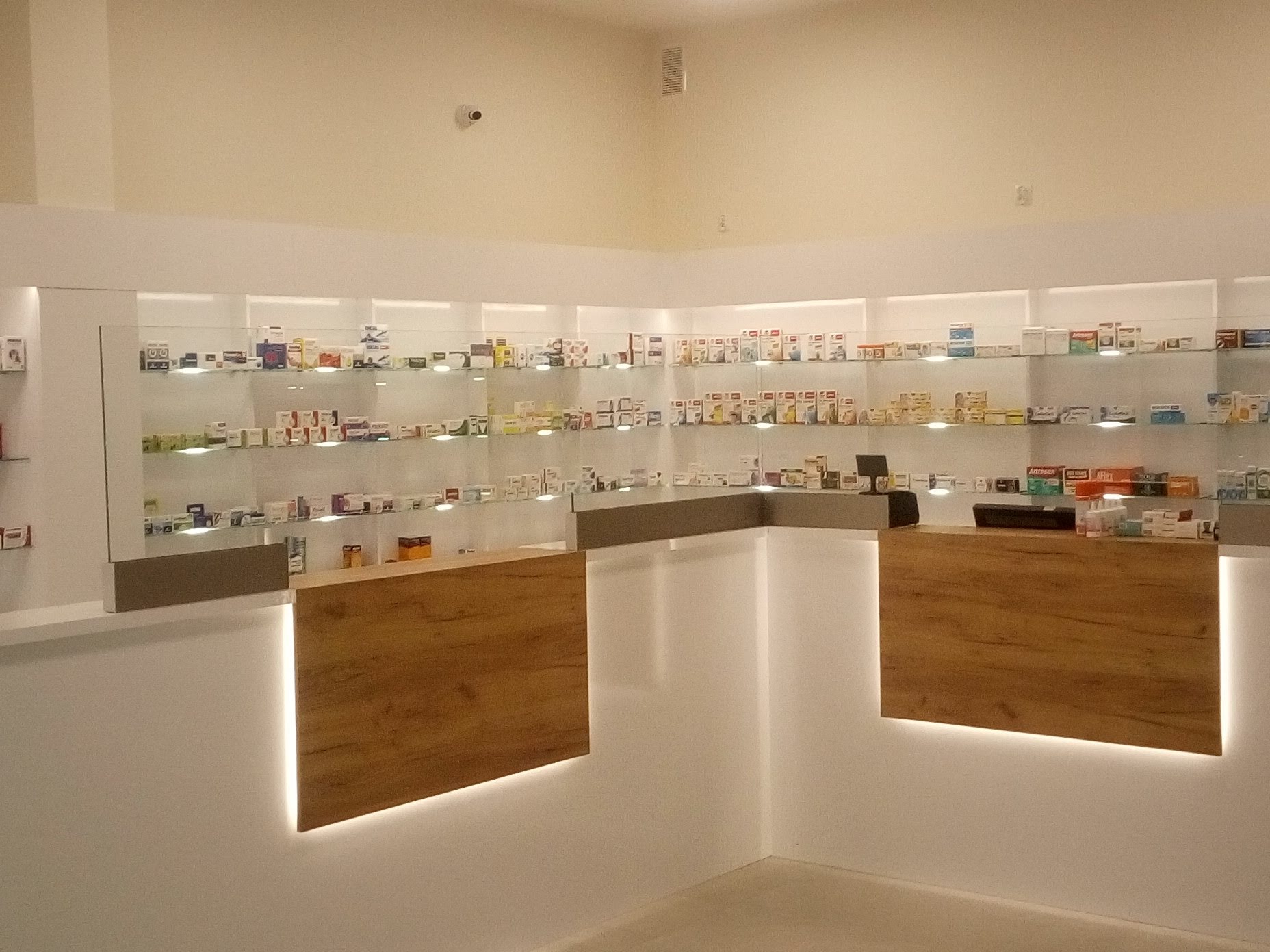 Apteka z drewnianymi ladami podświetlonymi LED i szklanymi półkami z lekami. Minimalistyczny design, równomierne oświetlenie, jasne wnętrze. Widok z perspektywy klienta.