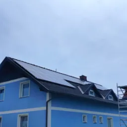 Niebieski dom z panelami słonecznymi na dachu, widoczne rusztowanie z boku.