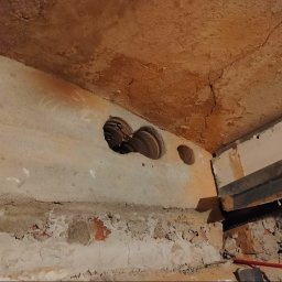 ETP Solution - Wykute otwory w ścianie pod instalacje w starym budynku z cegły, widoczny fragment belki stropowej.