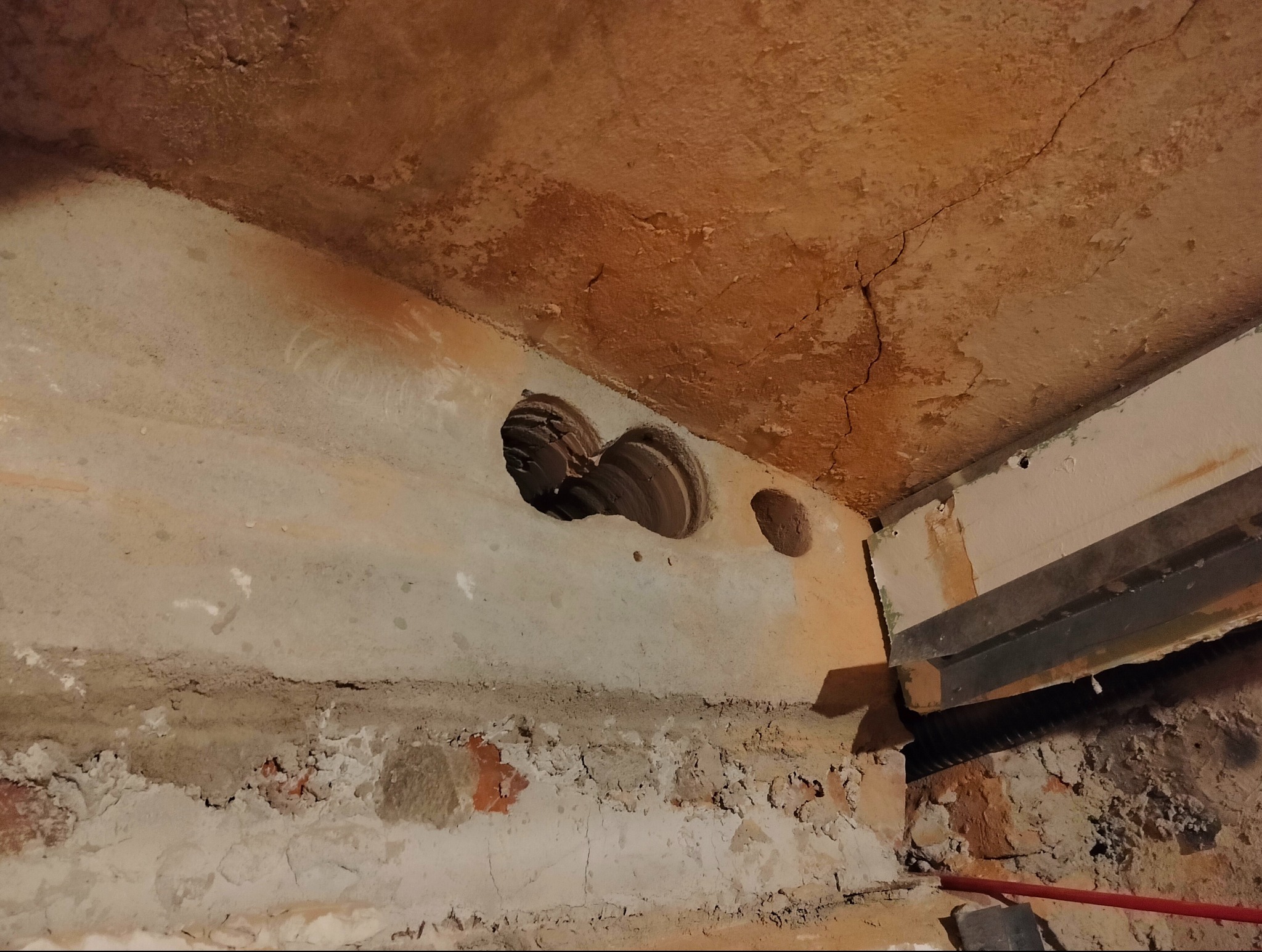 Wykute otwory w ścianie pod instalacje w starym budynku z cegły, widoczny fragment belki stropowej.